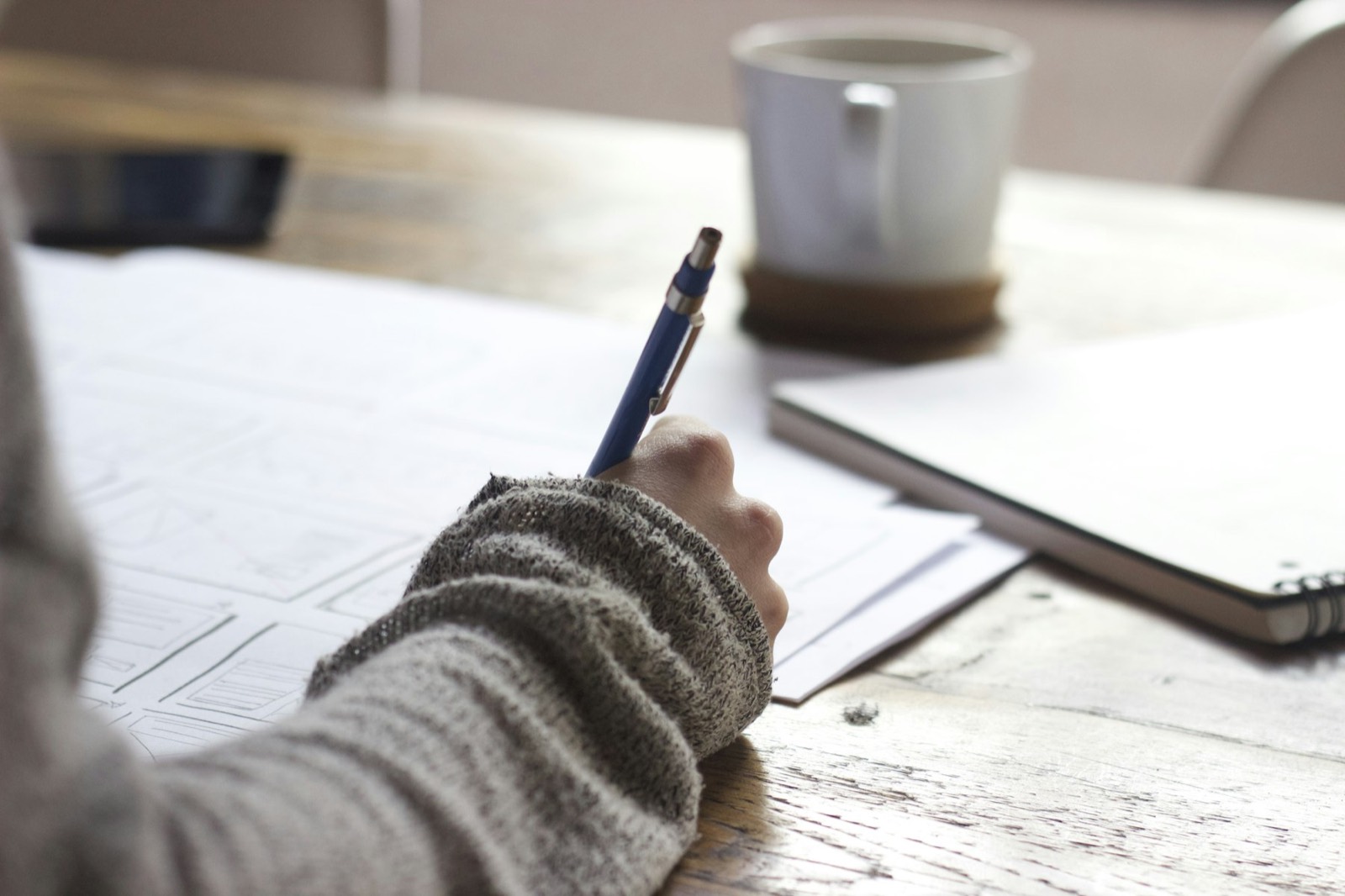 Writing notes at a timber desk beside a cup of coffee